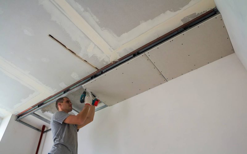 Construction worker assemble a suspended ceiling with drywall and fixing the drywall to the ceiling